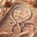 Collar de perlas con lazo central dorado sobre tela rosa con rosas