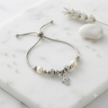 Pulsera perlas blancas con charm Mano de Fátima y aros strass sobre mármol con lavanda