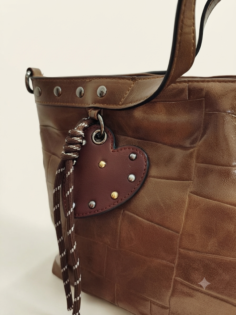 Detalle del bolso tote marrón con colgante de corazón y tiras decorativas