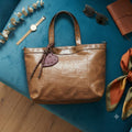 Bolso tote marrón con detalle de corazón, tachuelas y tiras decorativas