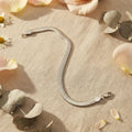 Pulsera plana tipo serpiente acero inoxidable plateado sobre tela beige con pétalos